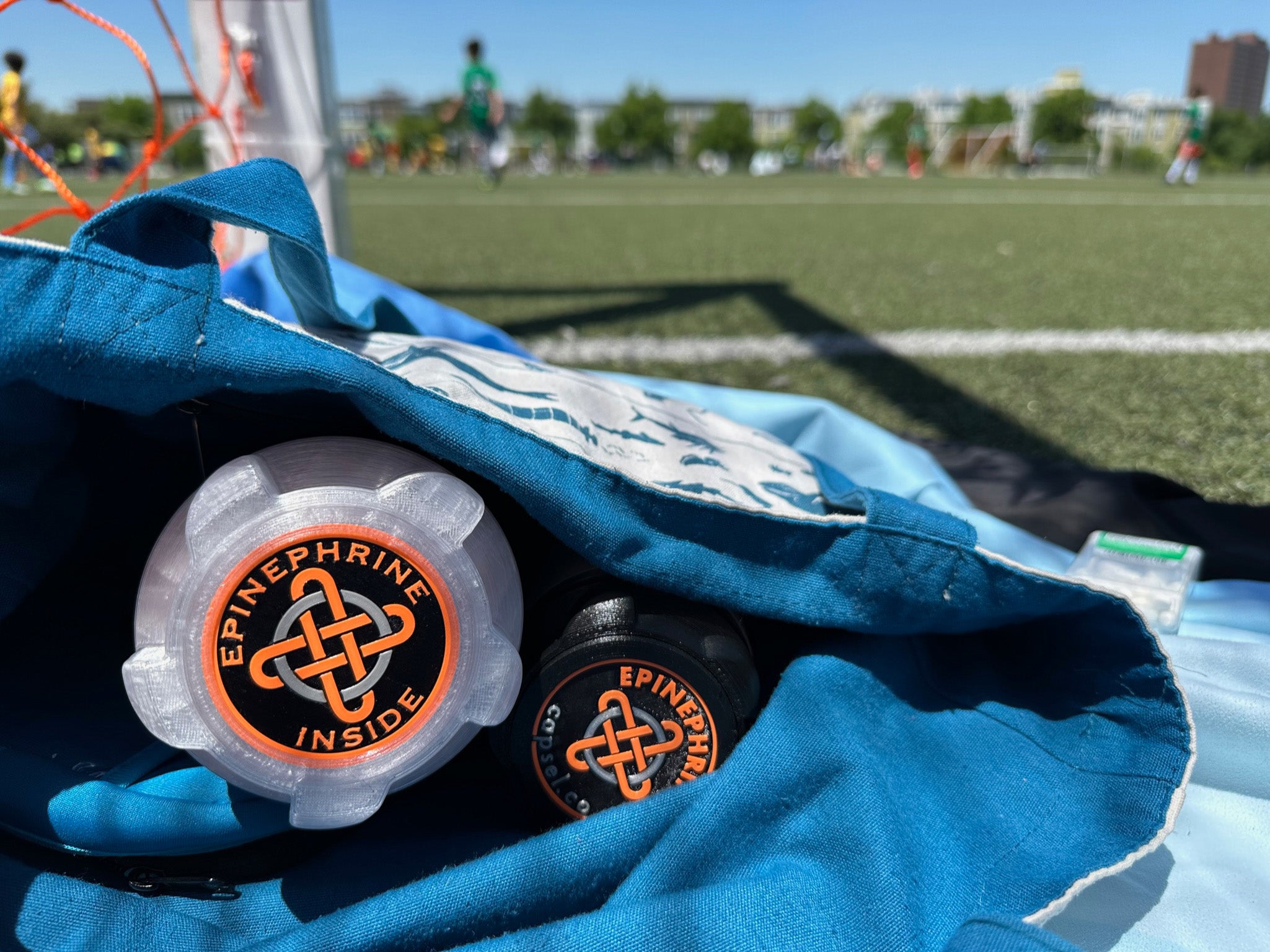Capsel™ epinephrine auto-injector cases in a bag at a sports field
